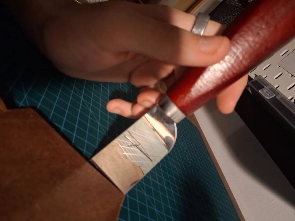 Image of leather hand stitching needles in reflection of leather cutting knife