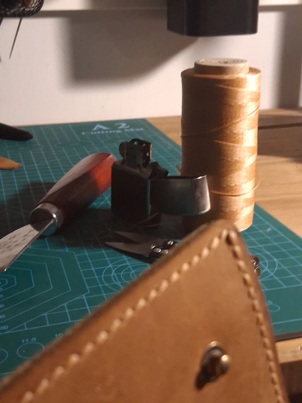 Image of leather wallet being held in stitching horse for hand stitching along with leatherworking tools on workbench
